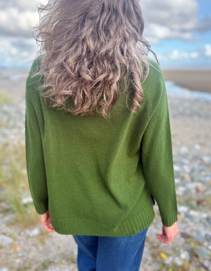 Person wearing a green sweater standing on a beach with a cloudy sky.