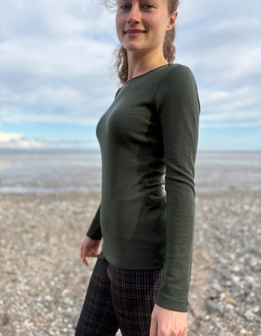 lady wearing fine merino long sleeve t shirt in moss green on a beach
