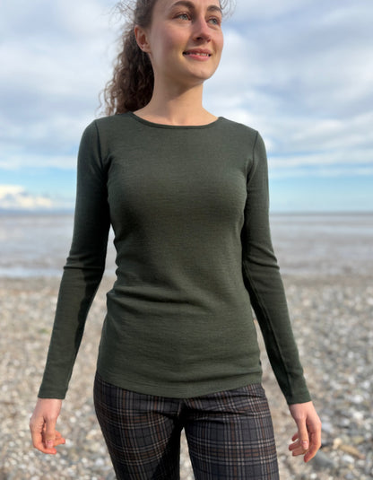 lady wearing fine merino long sleeve t shirt in moss green on a beach