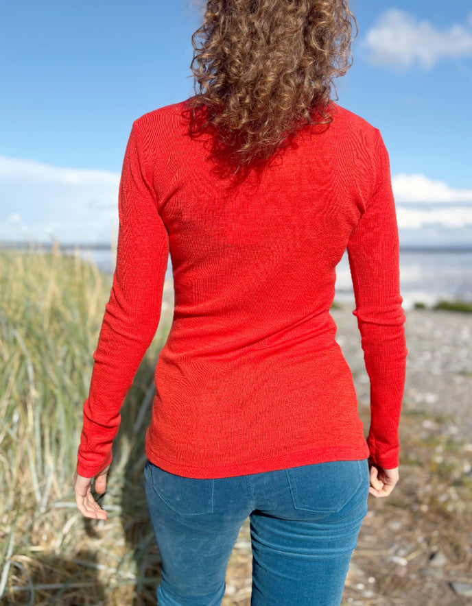 Woman wearing an orange fine merino long sleeve t shirt standing outdoors with a blue sky and clouds in the background