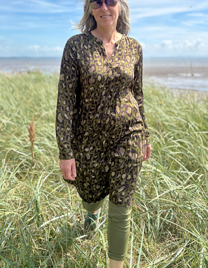 Person wearing a leopard print dress standing on a grassy field with a beach and blue sky in the background