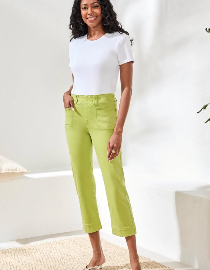 Woman wearing a white top and green pants in a bright room