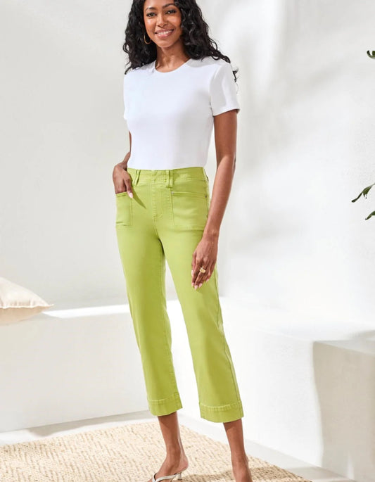Woman wearing a white top and green pants in a bright room