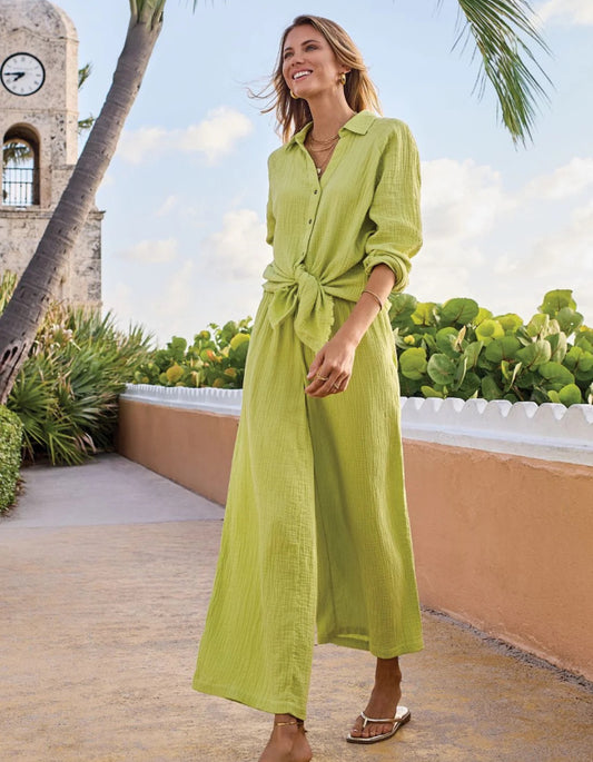 Woman in a green coord trouser and blouse standing on a rooftop with palm trees and a clock tower in the background.