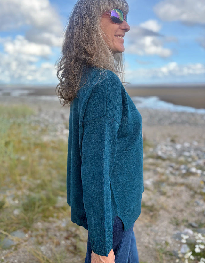 Woman wearing a teal sweater standing in a field with a blue sky.