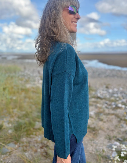 Woman wearing a teal sweater standing in a field with a blue sky.