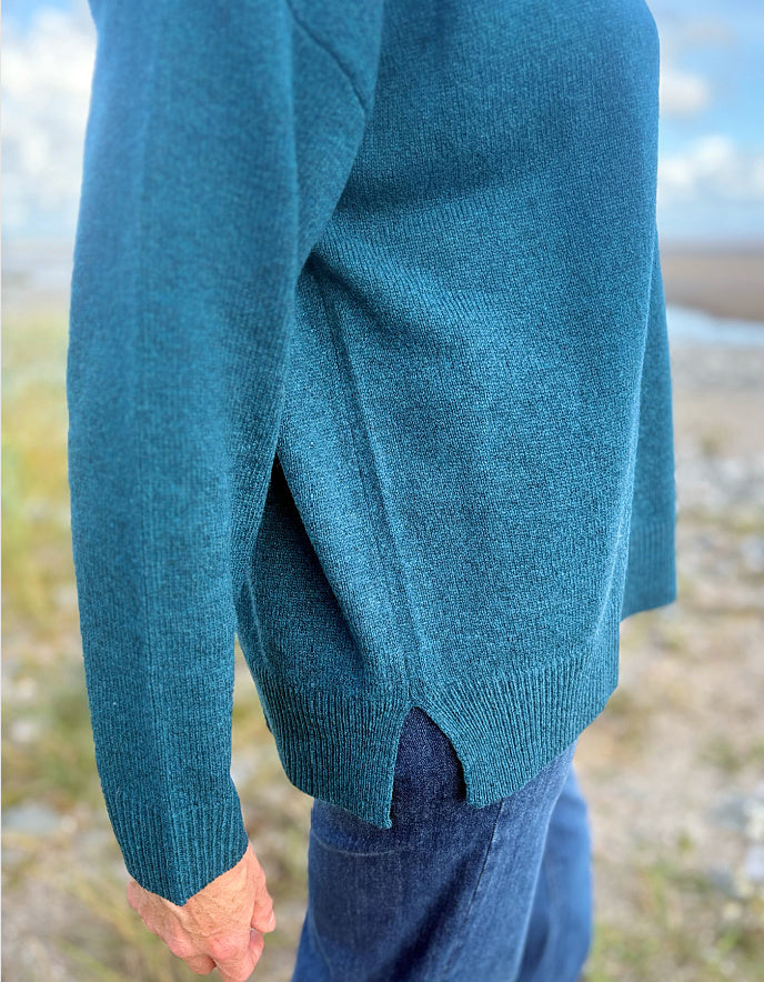 Teal sweater worn by a person with a blurred natural background