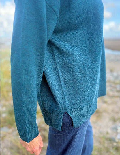 Teal sweater worn by a person with a blurred natural background