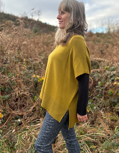 Woman wearing a yellow poncho standing in a field with dry grass and wildflowers.