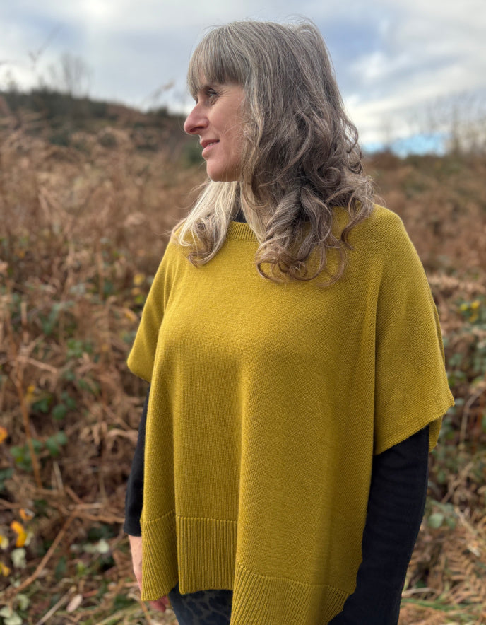Woman wearing a yellow sweater standing in a field with a cloudy sky.