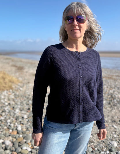 Woman wearing a dark blue cardigan and sunglasses on a beach.