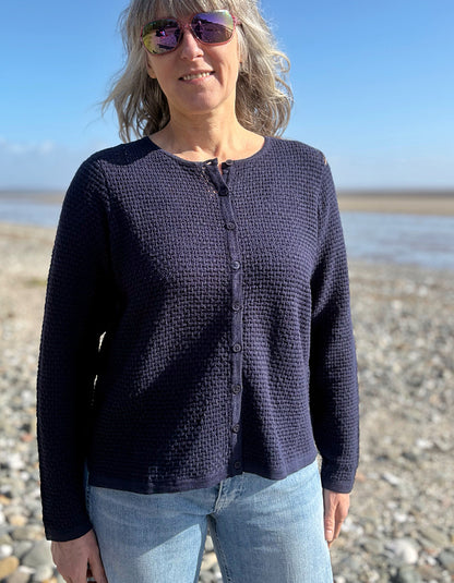 Woman wearing a dark blue cardigan and sunglasses on a beach.