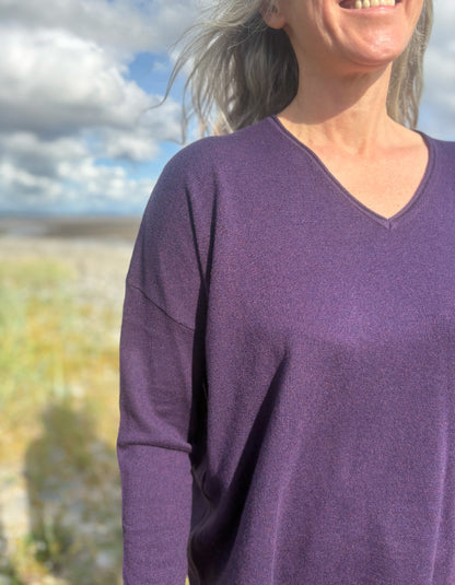 Person wearing a purple V neck merino sweater with a blurred natural background