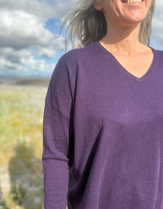 Person wearing a purple V neck merino sweater with a blurred natural background