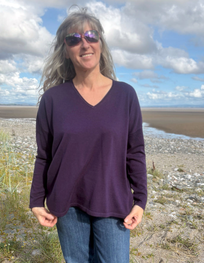 Person wearing a purple V neck merino sweater with a blurred natural background