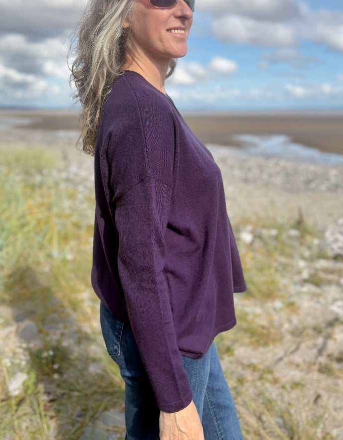 Person wearing a purple V neck merino sweater with a blurred natural background