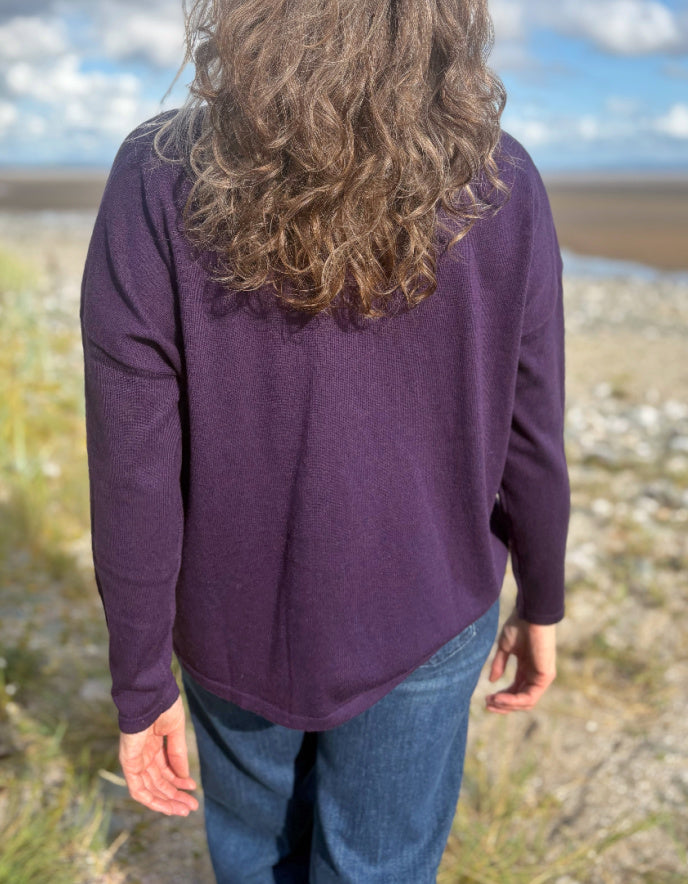 Person wearing a purple V neck merino sweater with a blurred natural background