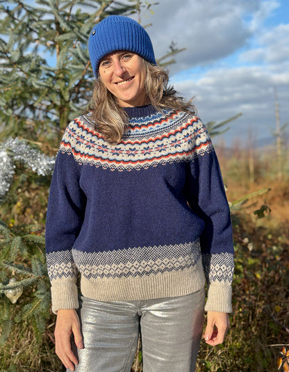 Person wearing a fair Isle patterned sweater and colourful hat standing outdoors with trees in the 