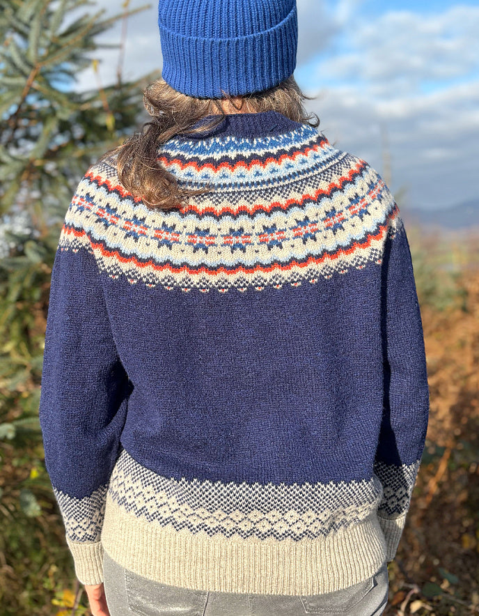 Person wearing a fair Isle patterned sweater and colourful hat standing outdoors with trees in the 