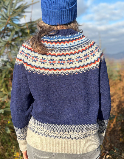 Person wearing a fair Isle patterned sweater and colourful hat standing outdoors with trees in the 