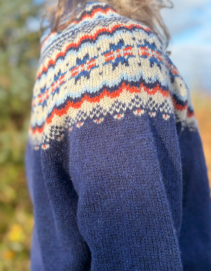 Navy blue sweater with colorful patterned shoulders against a blurred natural background
