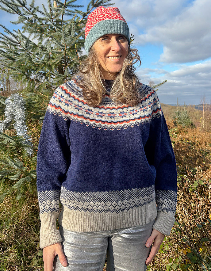 Person wearing a fair Isle patterned sweater and colourful hat standing outdoors with trees in the background