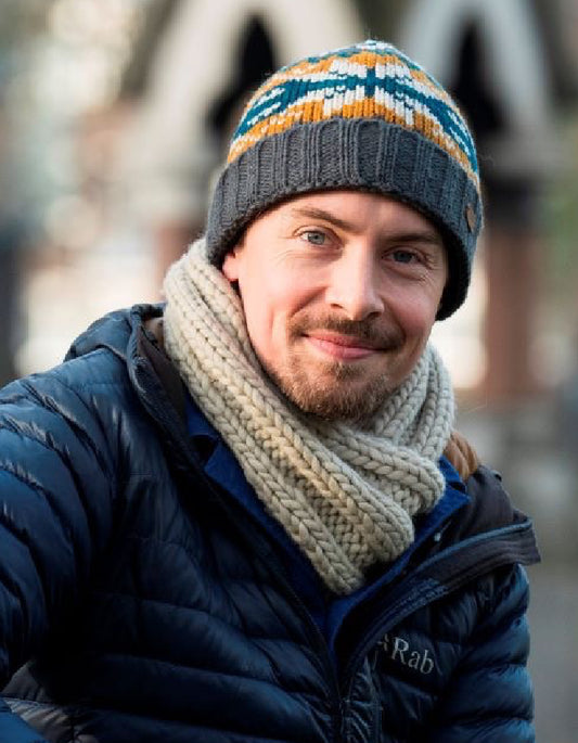 Man wearing a colorful knit hat and scarf with a blurred background