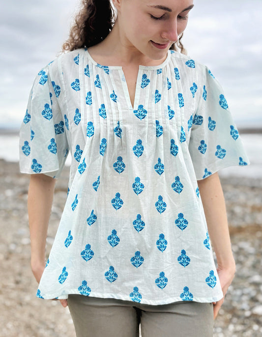 Woman wearing a white blouse with blue floral patterns on a beach.
