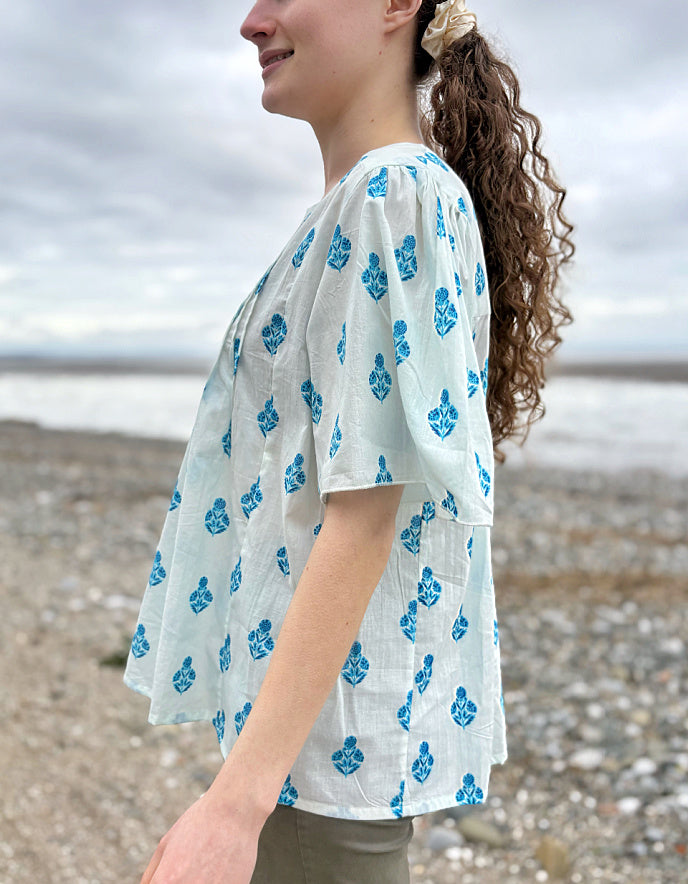 Woman wearing a light blue kimono-style garment with blue floral patterns on a beach.