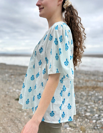Woman wearing a light blue kimono-style garment with blue floral patterns on a beach.