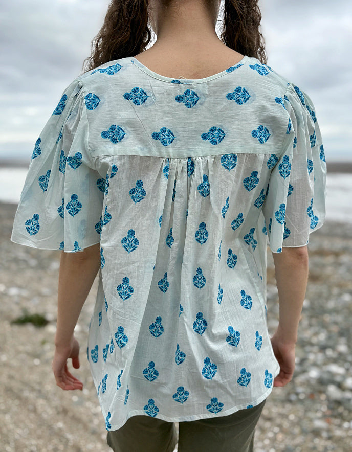 Person wearing a white blouse with blue floral patterns on a beach.