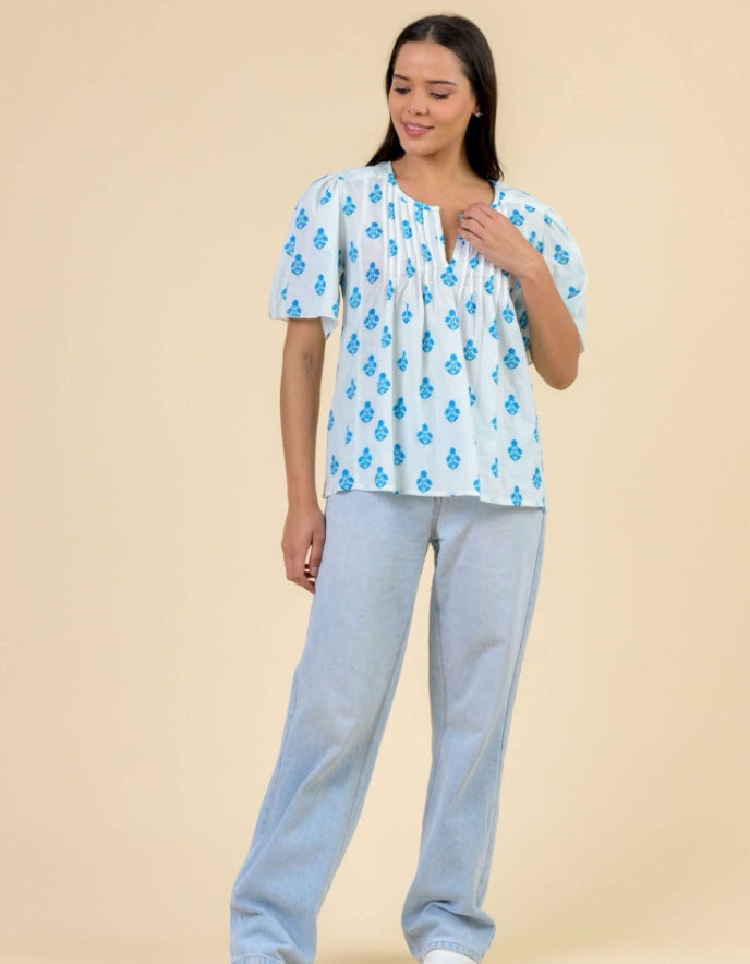 Woman wearing a blue floral top and light gray pants on a beige background