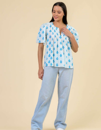 Woman wearing a blue floral top and light gray pants on a beige background