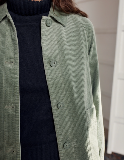 Person wearing sage green boxy fit cotton cord jacket with a white background