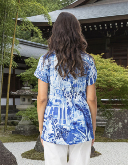 Woman wearing a blue patterned shirt standing in front of a traditional building with bamboo and stone lanterns.