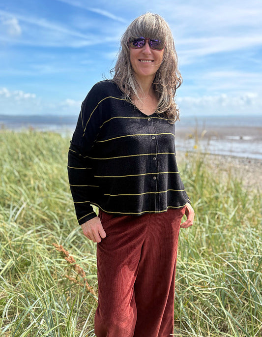 Person wearing a black and yellow striped sweater and red pants standing in a grassy field with a beach in the background.