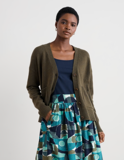 Woman wearing a green cardigan, navy top, and patterned skirt on a white background