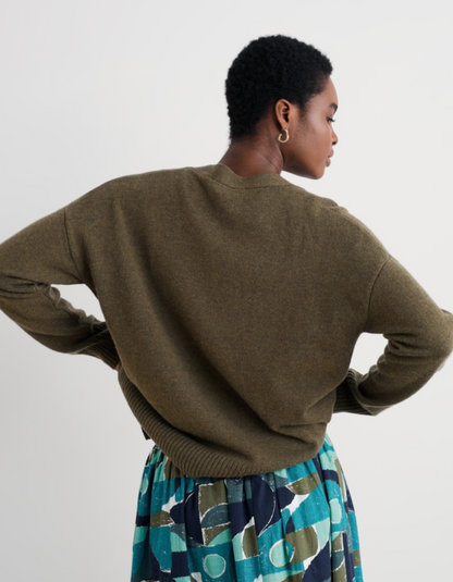 Person wearing a brown sweater and patterned skirt on a plain background