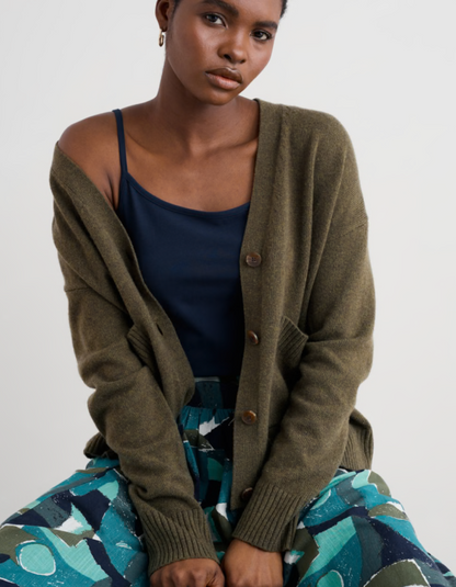 Woman wearing a green cardigan over a blue top and patterned skirt on a white background