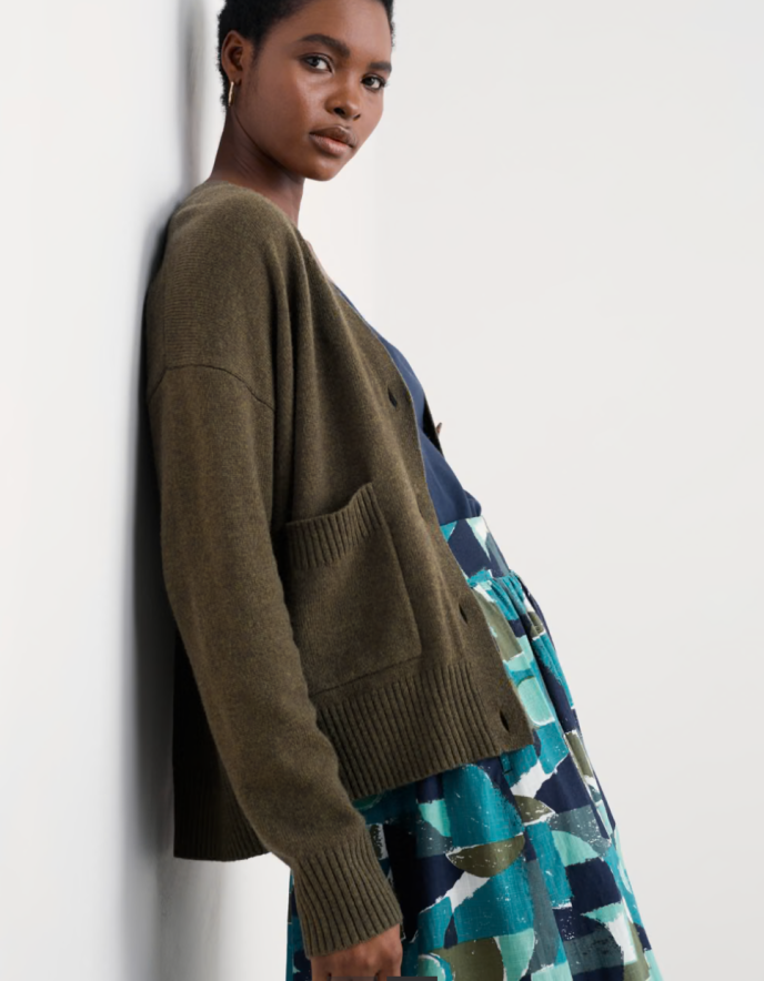 Woman wearing a green cardigan over a patterned dress against a white background