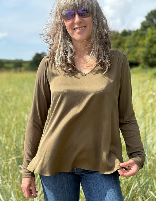 Woman wearing a brown long-sleeve top and sunglasses, standing in a field.