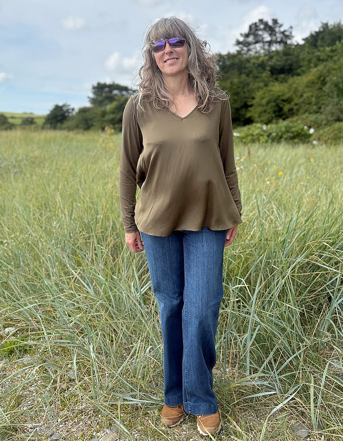 Woman standing in a field wearing a brown top and blue jeans.