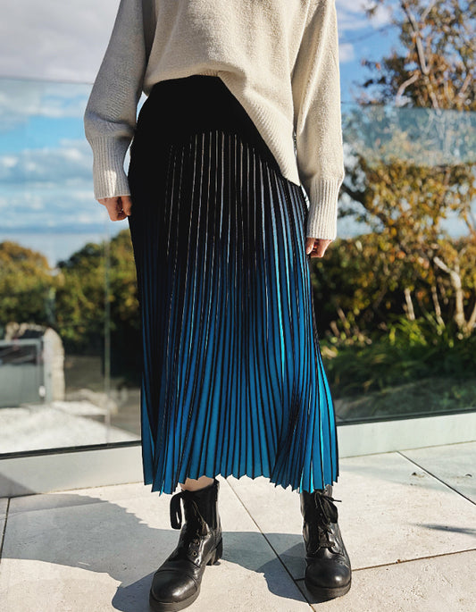 Person wearing a turquoise and black ombre pleated skirt and black boots outdoors. 