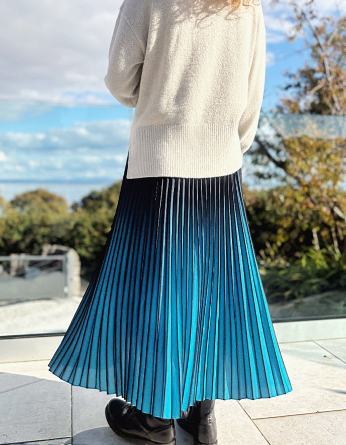 Person wearing a turquoise and black ombre pleated skirt and black boots outdoors. 