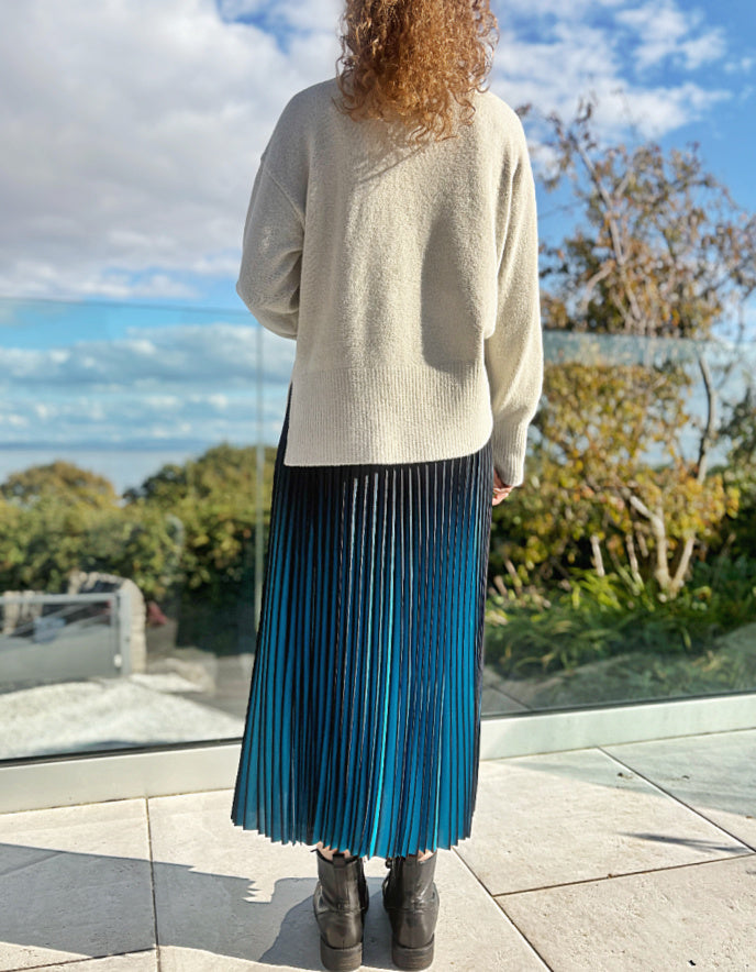 Person wearing a turquoise and black ombre pleated skirt and black boots outdoors. 