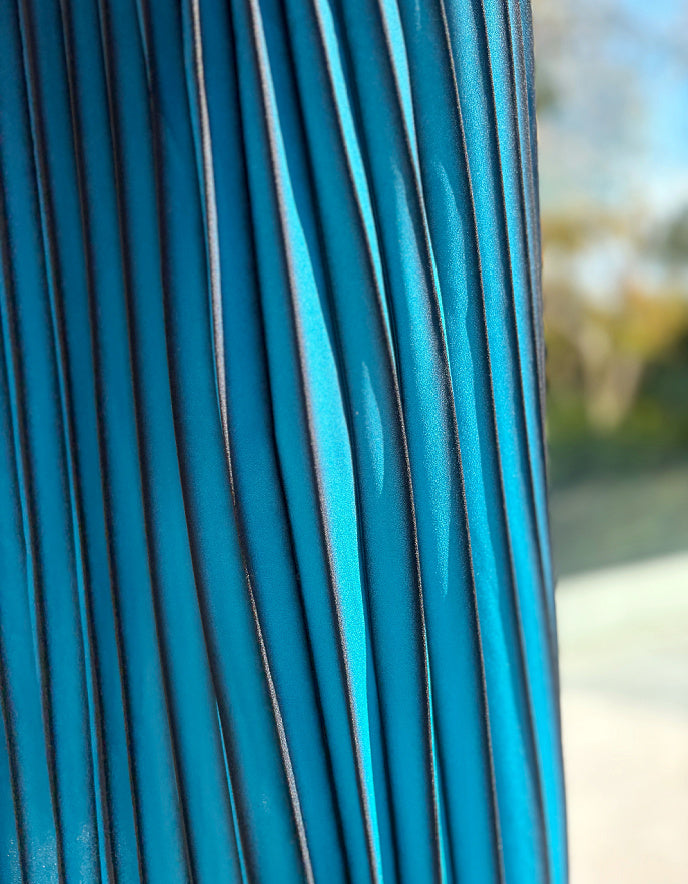 Person wearing a turquoise and black ombre pleated skirt and black boots outdoors. 