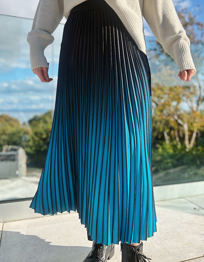 Person wearing a turquoise and black ombre pleated skirt and black boots outdoors. 