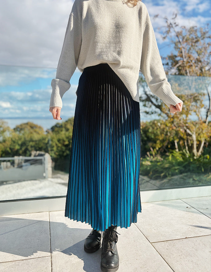 Person wearing a turquoise and black ombre pleated skirt and black boots outdoors. 
