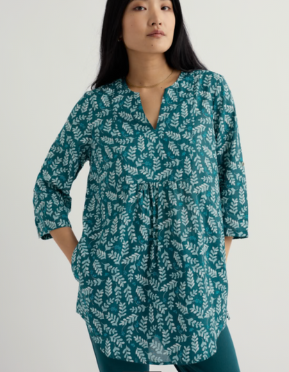 Woman wearing a teal dress with white floral pattern on a plain background