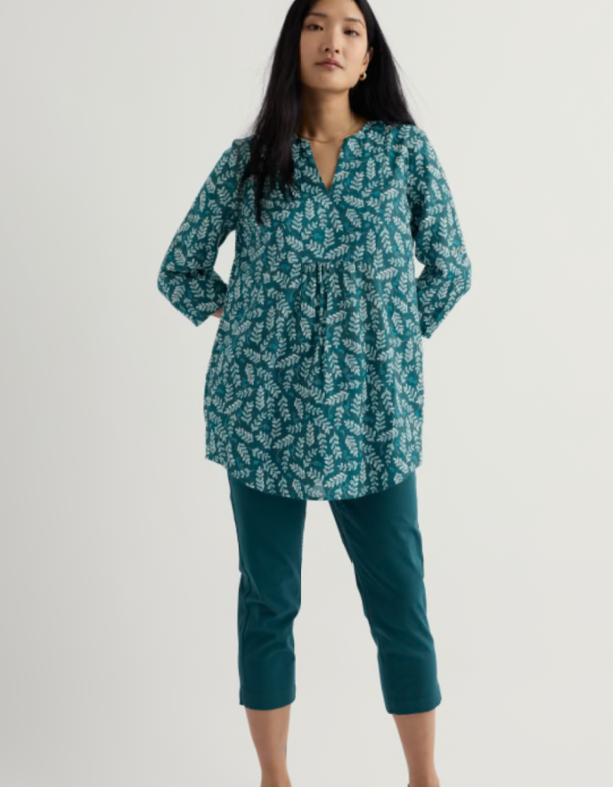 Woman wearing a teal patterned blouse and pants on a white background